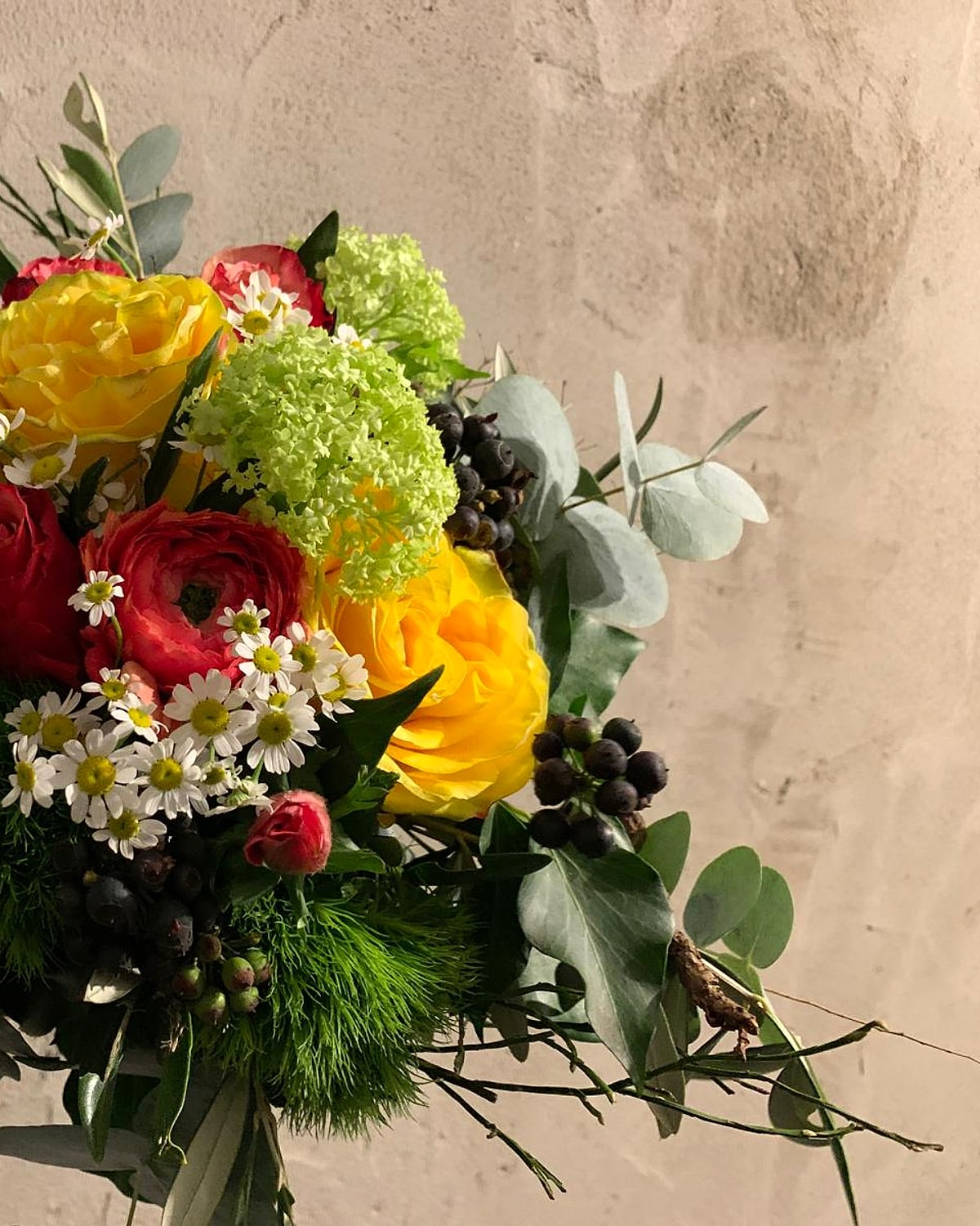Farbenfroher Blumenstrauß mit gelben und roten Rosen vor einer Natursteinwand