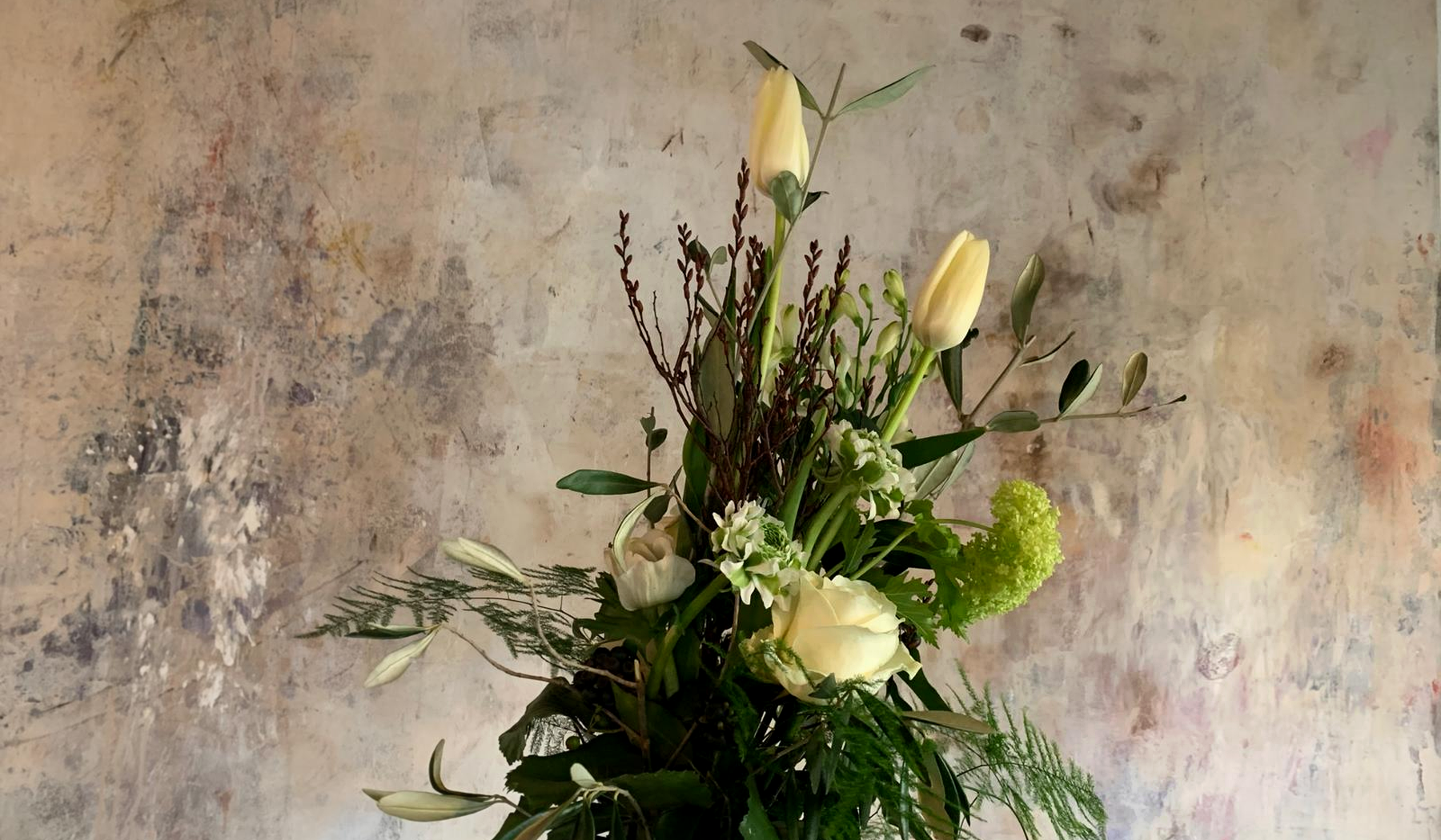 Florales Gesteck mit hellen Blüten vor einer strukturierten Wand