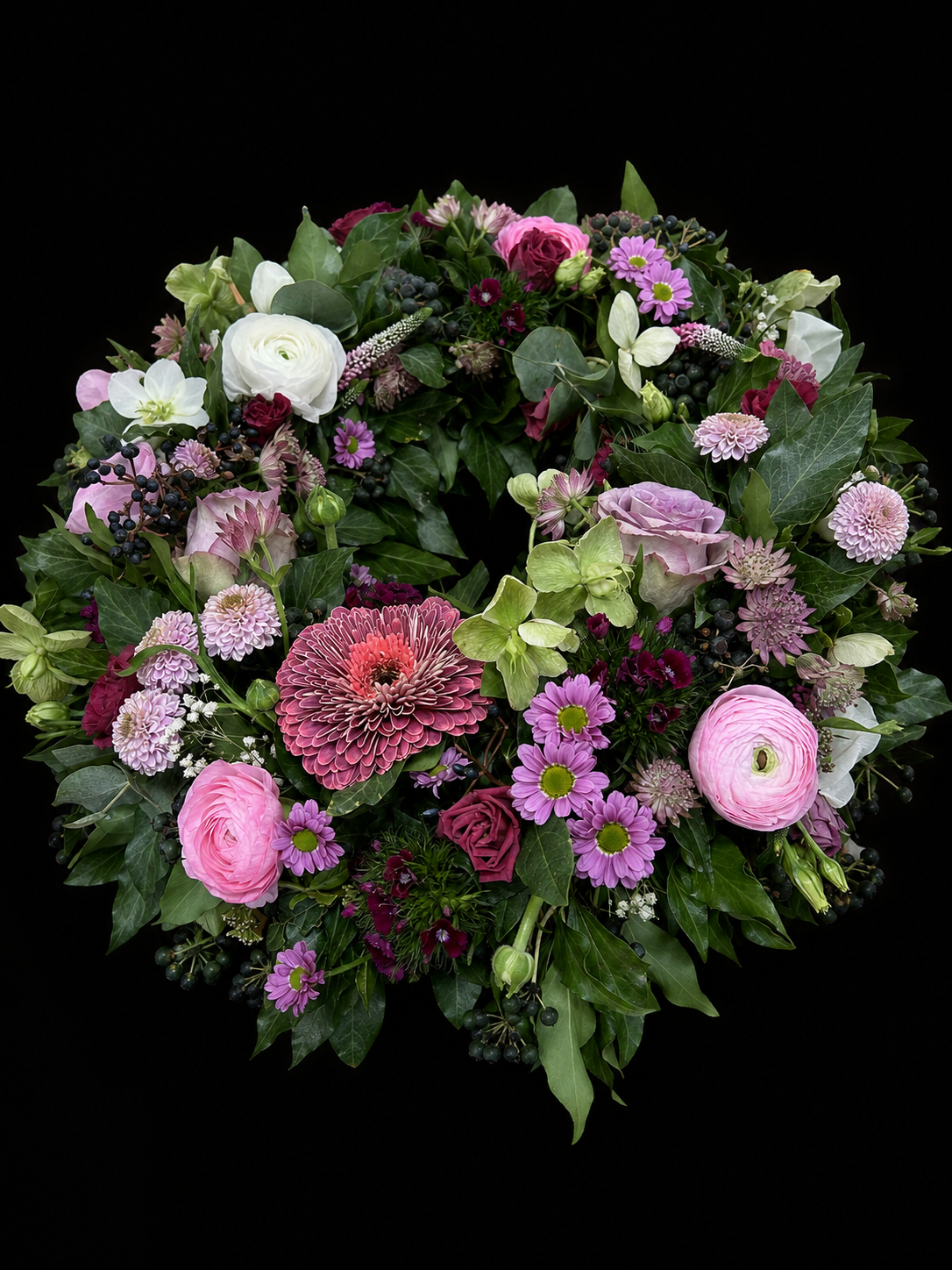 Floraler Trauerkranz in Rosé, Mauve und tiefem Grün vor schwarzem Hintergrund